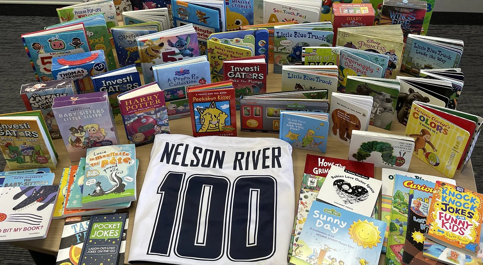 Hundreds of children's books surrounding a hockey jersey with the words: Nelson RIver 100