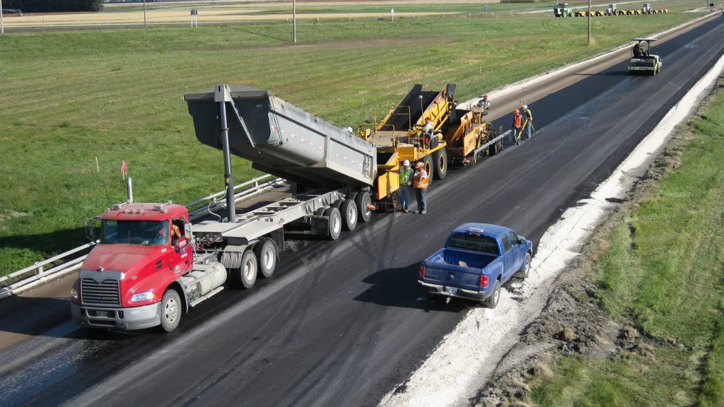An aerial view of a large dump truck filling a paving machine with asphalt
